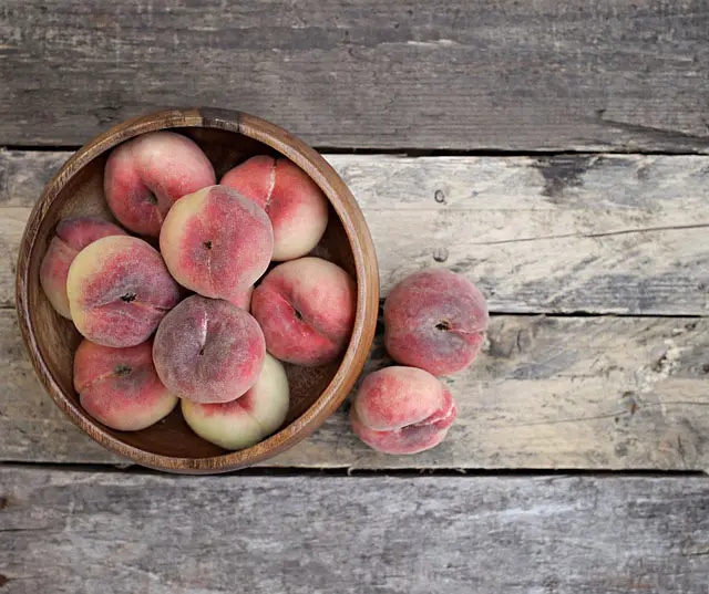 Image of ripe peaches in a bowl on a wooden table.