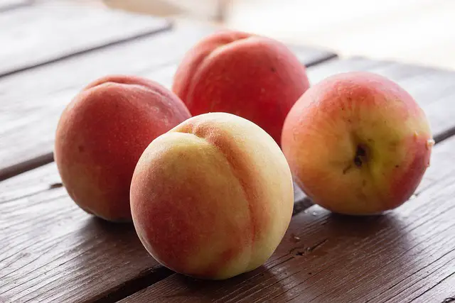 Image of four yellow-red peaches on a wooden table.