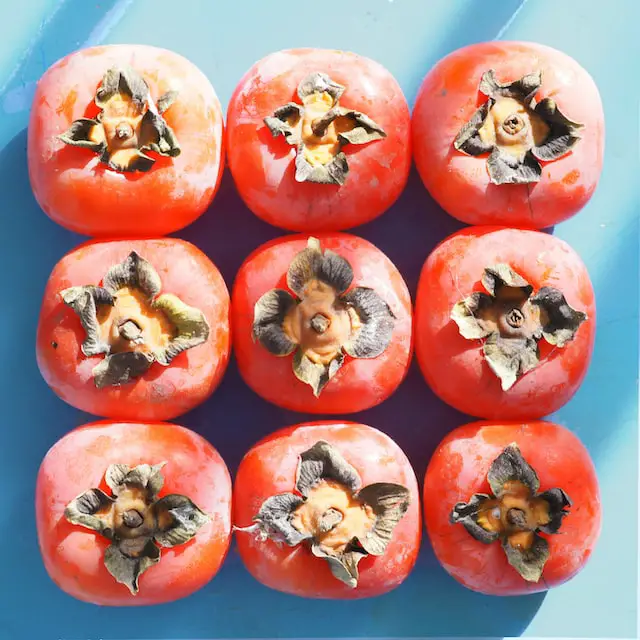 Image of nine, ripe, red-orange persimmons arranged in a grid.
