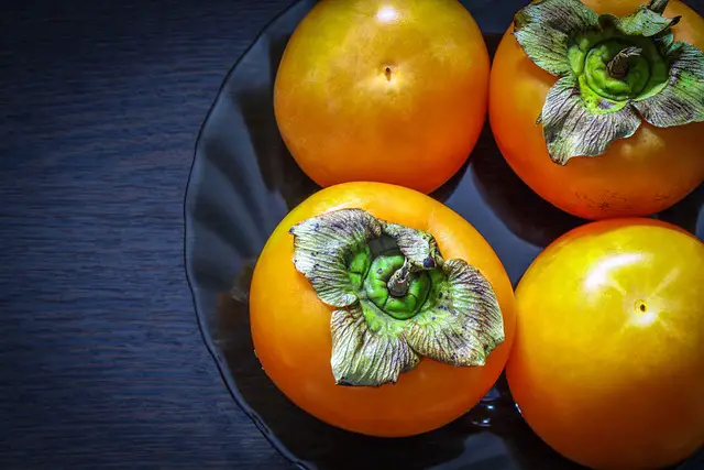 Image of ripe orange persimmons in a black bowl.