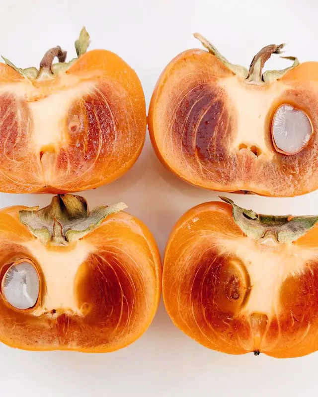 Image of two seeded, persimmons with dark orange flesh. The darker flesh and seeds show that this is a pollination-variant type of persimmon.
