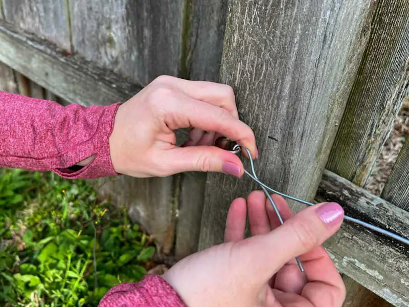 Image of a woman's hands twisting wire through an eye screw that is attached to a fence post.